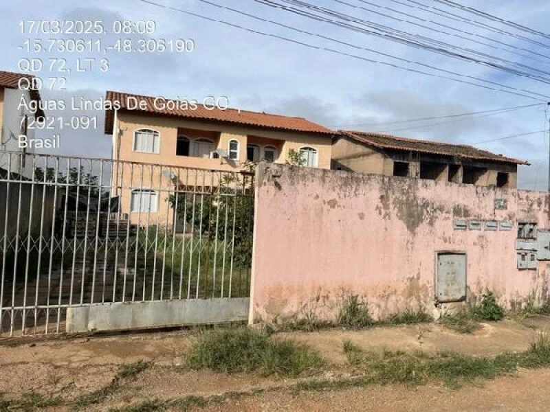 Apartamento bege de 2 andares com grade frontal e muro rosa gasto localizado em área residencial com vegetação ao redor