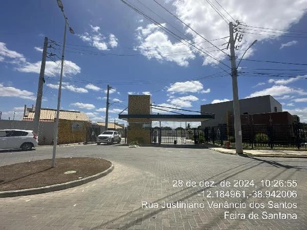 Casa em condomínio com portaria de segurança, muro com grades e área pavimentada sob céu azul