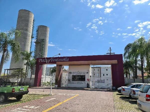 Apartamento em condomínio residencial com portaria e entrada principal visível em dia claro com carros estacionados