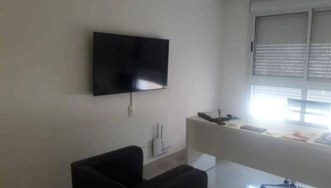 Apartamento branco com sofá preto, TV de tela plana na parede e janela com persiana em ambiente interno claro