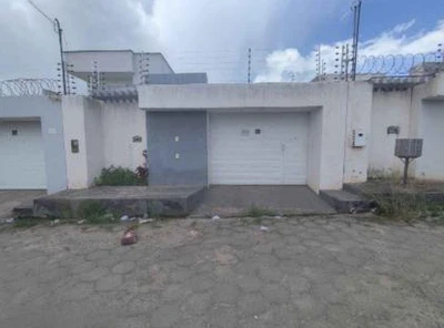 Casa branca com portão e garagem, fachada simples em rua pavimentada, sem danos visíveis.