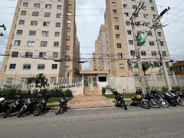 Apartamento bege em condomínio residencial com grade e portaria, várias motos estacionadas na rua em frente