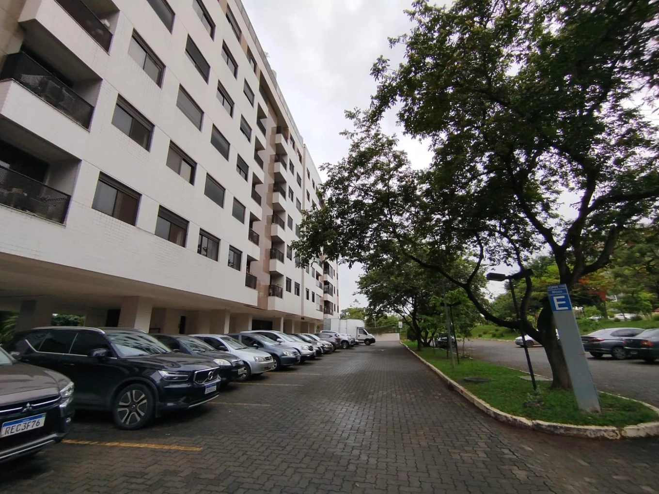 Apartamento branco de 7 andares com vagas de estacionamento na frente e árvores ao redor