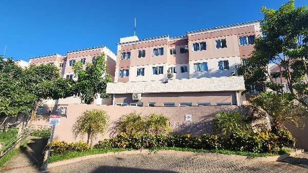 Apartamento bege em condomínio residencial com três andares e jardim frontal bem cuidado