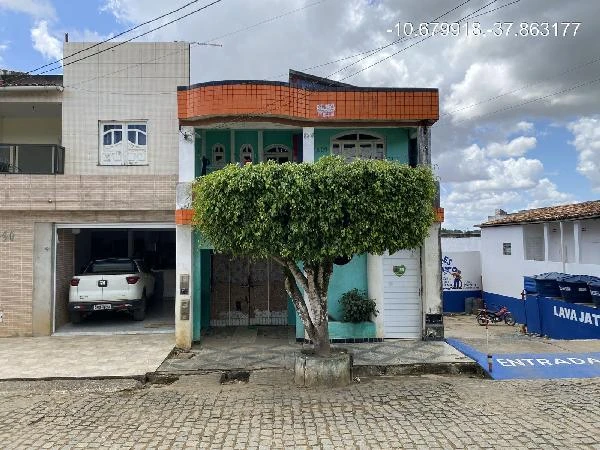 Apartamento verde com varanda, 2 andares, fachada com detalhes laranja, localizado em rua com paralelepípedos