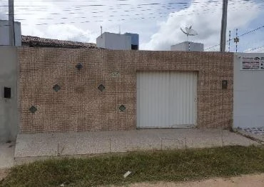Casa com fachada em parede revestida de tijolos aparentes e portão branco em área residencial