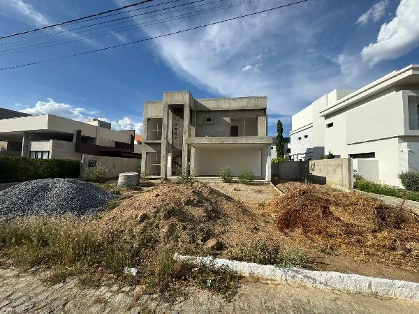 Casa cinza em construção de dois andares com fachada sem pintura em condomínio residencial com áreas vizinhas construídas e terreno com terra e entulho na frente