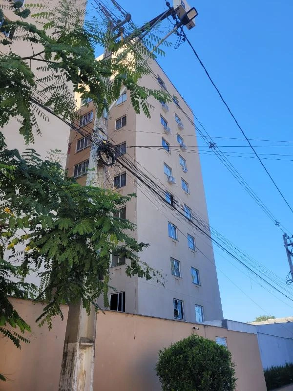 Apartamento bege de 50m² com 2 quartos em condomínio residencial visto de fora com muro e vegetação ao redor
