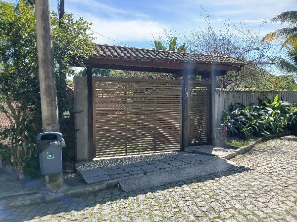 Casa com portão de madeira e garagem em área residencial com vegetação ao redor