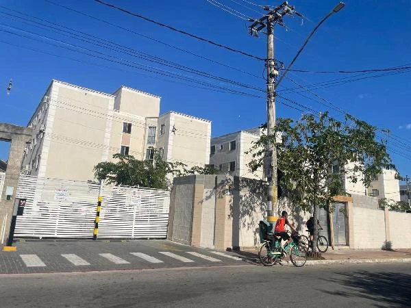 Apartamento bege com três andares e portão branco em condomínio durante o dia com ciclistas próximos