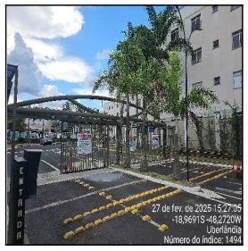 Apartamento branco com fachada de prédio residencial e portão de entrada em área urbana com árvores