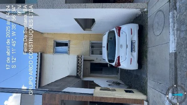 Casa branca com garagem pequena e veículo estacionado em área pavimentada de condomínio residencial