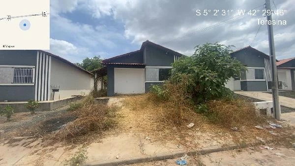 Casa cinza com 2 quartos e varanda, fachada com áreas de vegetação e calçada em frente, em área residencial de Teresina