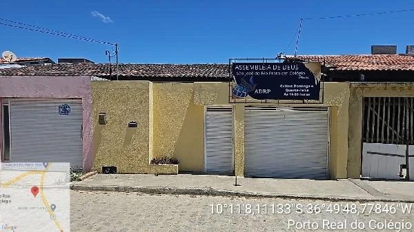 Casa amarela com porta e garagem de metal em rua com calçamento irregular em loteamento residencial