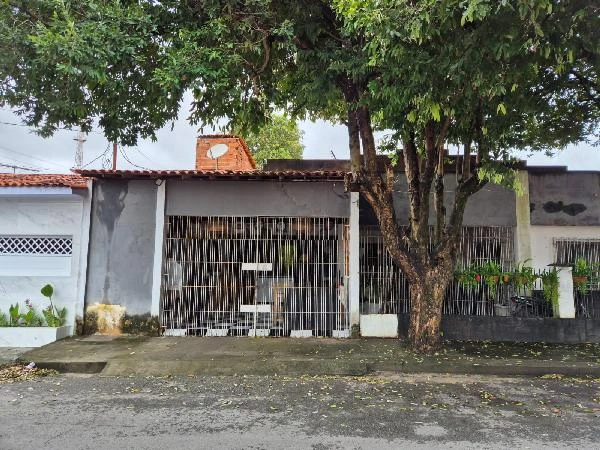 Casa cinza com grade branca na fachada e árvore grande em frente na rua residencial