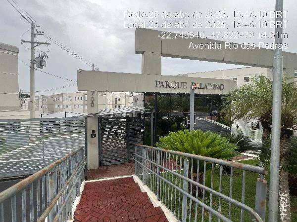 Entrada do condomínio residencial Parque Paladino com acesso para pedestres, grade metálica e vegetação no local em dia nublado