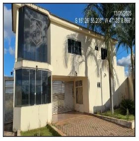 Casa branca de dois andares com varanda envidraçada, garagem descoberta e jardim frontal sob luz natural