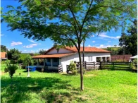 Sítio com casa sede branca, área verde com árvores e cercas em local rural com céu azul