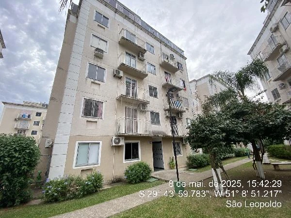 Apartamento bege de 93m² em condomínio com quatro andares, varandas pequenas e área verde ao redor visualizado em dia nublado
