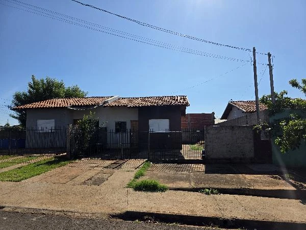 Casa branca com telhado de cerâmica, portão de ferro e jardim frontal em área residencial ensolarada