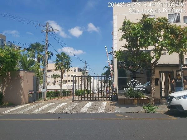 Apartamento branco em condomínio residencial Spazio Rio Pérola com portão de entrada e vagas de garagem visíveis em área urbana