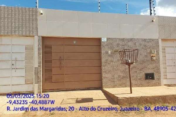Casa com fachada bege e portão marrom, garagem e muros revestidos em cerâmica em área residencial
