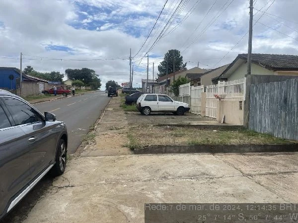 Casa residencial com muro branco e portão em bairro urbano, garagem descoberta, calçada e rua asfaltada