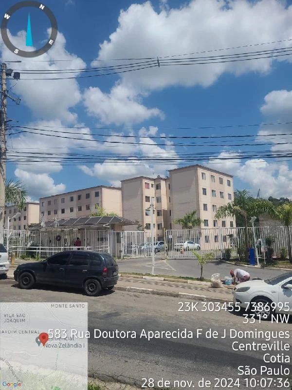 Apartamento residencial bege com quatro pavimentos e área externa com guarita e cerca metálica em rua urbana