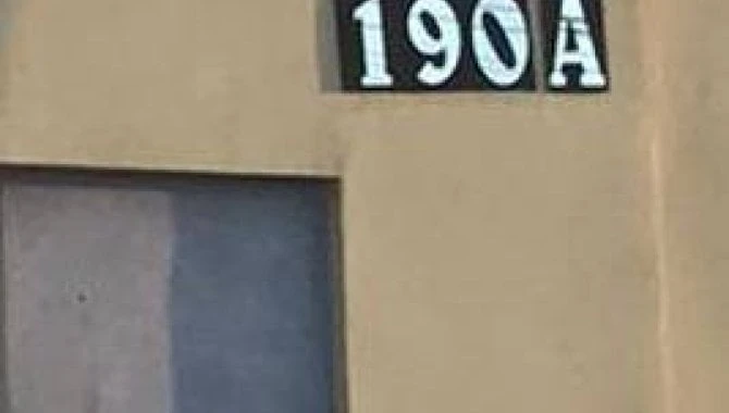 Casa com pintura bege, porta de madeira ao lado da numeração 190A, fachada sem avarias visíveis
