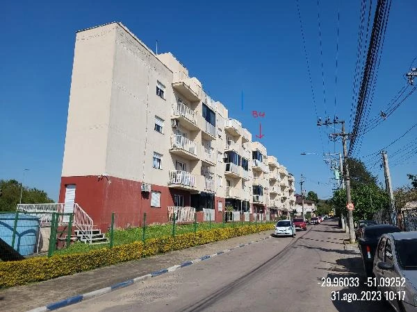 Apartamento branco com detalhes vermelhos em condomínio residencial de quatro andares na rua asfaltada com carros estacionados