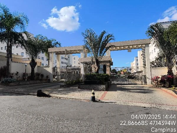 Apartamento residencial branco com 2 quartos e vaga de garagem visto pela entrada do condomínio com portaria e áreas ajardinadas
