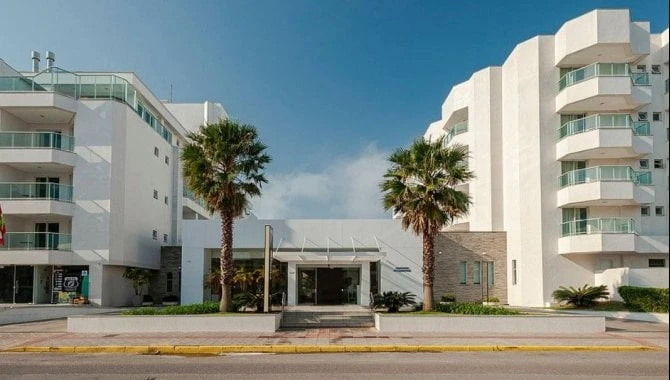 Apartamento branco com sacadas com vidro em condomínio residencial com entrada principal e palmeiras na fachada