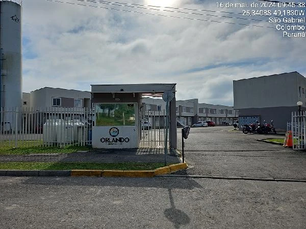 Entrada do condomínio residencial Orlando com guarita e casas em série ao fundo em área pavimentada
