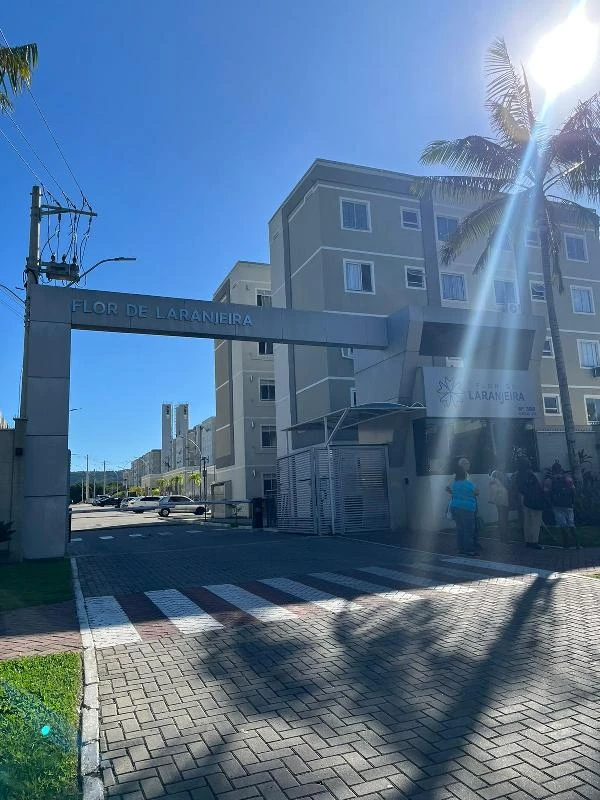 Apartamento cinza de 45m² no conjunto residencial Flor de Laranjeira com entrada e guarita em dia ensolarado