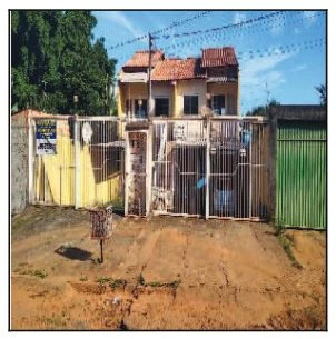 Apartamento amarelo com dois andares, portão branco de grade na frente em área residencial com terreno arenoso