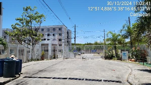 Apartamento branco de pequeno porte com portão de entrada em condomínio residencial e área externa pavimentada