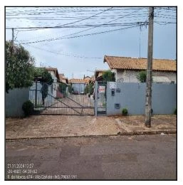 Casa cinza com portão de metal em condomínio residencial sob nuvens, fachada sem avarias visíveis