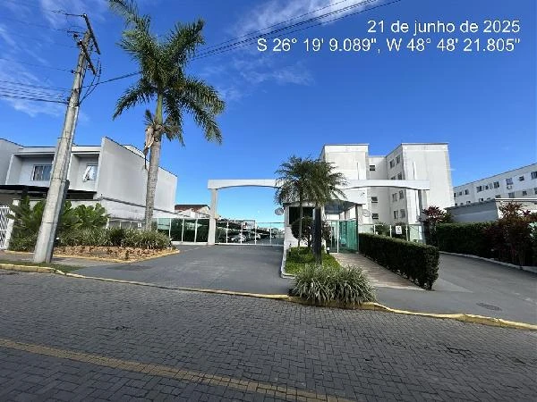 Apartamento branco em condomínio fechado com portaria e área externa pavimentada sob céu azul