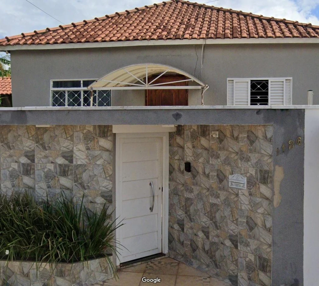 Casa cinza com porta branca e telhado de cerâmica em estado regular com fachada gradeada na rua