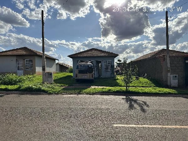 Casa branca simples com telhado de cerâmica e garagem aberta com veículo estacionado em área residencial