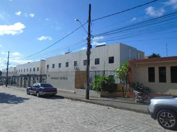 Apartamento branco com portão preto em condomínio residencial com veículos estacionados na rua de paralelepípedos
