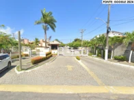 Casa duplex branca com porta principal em condomínio residencial com rua pavimentada e muro branco