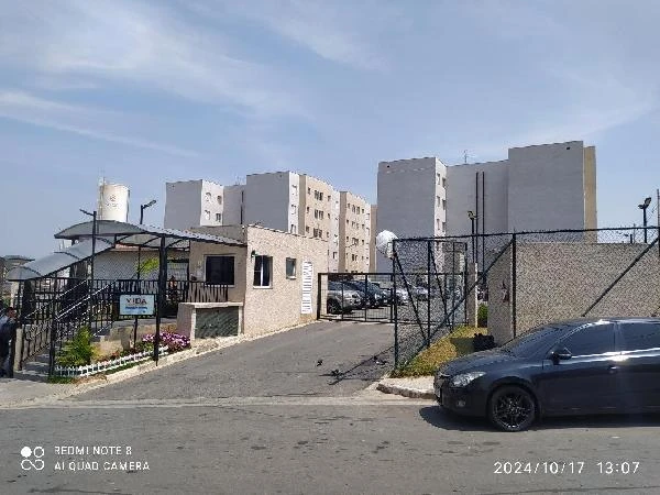 Apartamento branco com portaria em condomínio residencial e carro cinza estacionado na rua em frente
