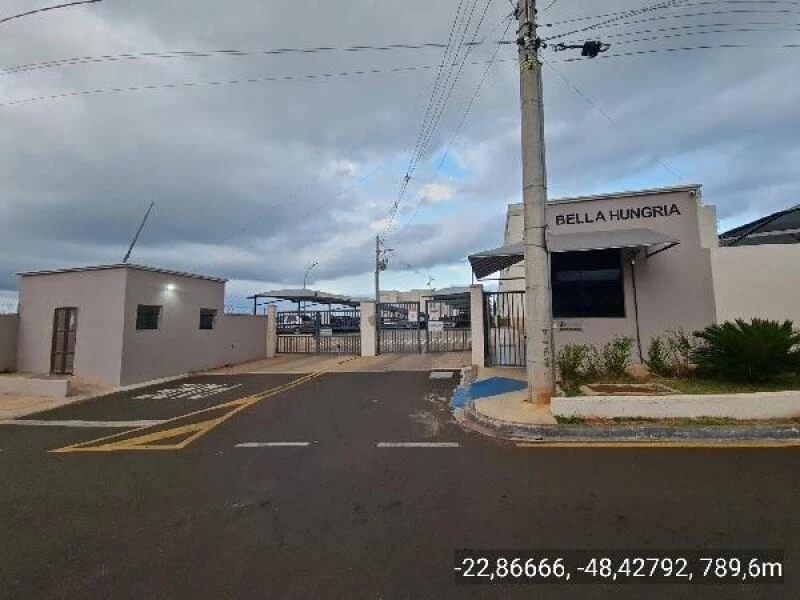 Entrada do condomínio residencial Bella Hungria em Botucatu com portaria e muro branco sob céu nublado