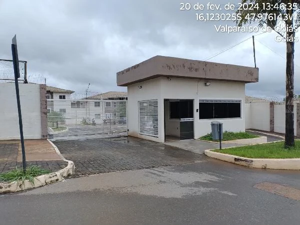 Apartamento branco em condomínio com guarita e portão automático em área urbana com pavimentação molhada
