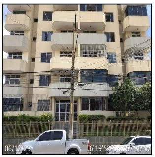 Apartamento bege em prédio com sacadas e grades, vista da fachada principal com veículo branco estacionado em frente