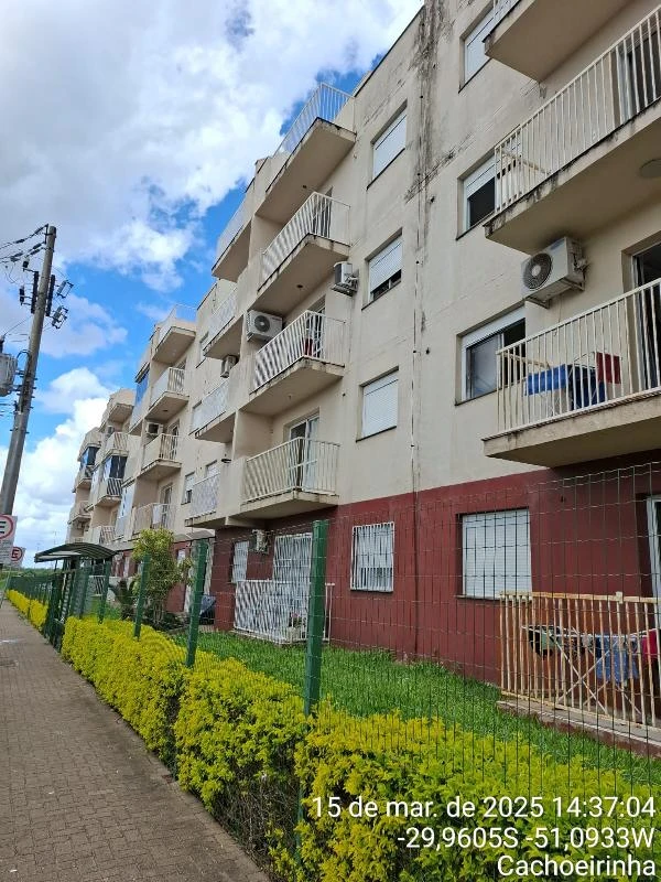 Apartamento branco com sacadas pequenas em condomínio residencial de três andares cercado por cerca metálica e área verde bem cuidada