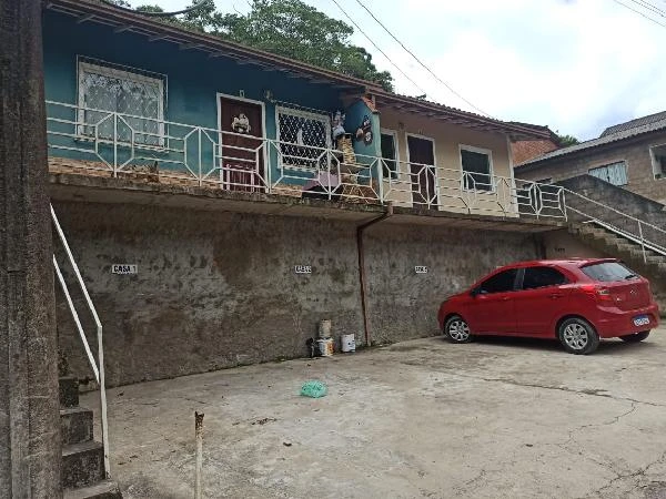 Casa de fachada simples com pintura azul e bege, varanda com grades metálicas, em área com estacionamento e carro vermelho