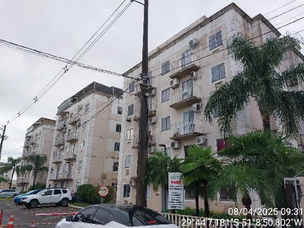 Apartamento bege com 3 quartos e varanda em prédio residencial de 4 andares, fachada com áreas de vegetação e veículos estacionados