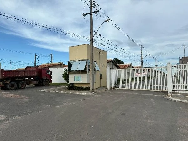 Casa branca no condomínio Plaza Das Flores Village 1 com portão branco e guarita de segurança em área pavimentada